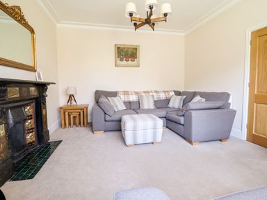 A living room with a grey sectional sofa and striped ottoman near a fireplace at Craigside in Betws-Y-Coed
