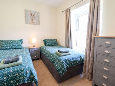 A bedroom with two single beds with teal bedding a nightstand with a lamp and a chest of drawers at Craigside in Betws-Y-Coed