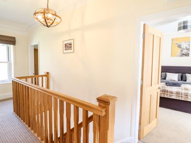A hallway with wooden stair railing and an open door leading to a bedroom with a bed at Craigside in Betws-Y-Coed