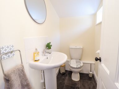 A bathroom with a sink a toilet a towel on a rack and a round mirror at Craigside in Betws-Y-Coed