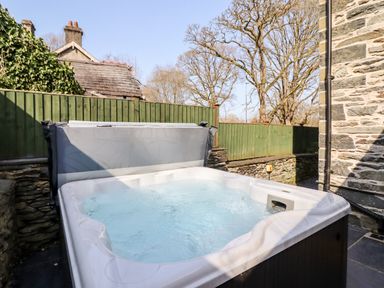 An outdoor hot tub with bubbling water next to a stone wall and green wooden fence at Craigside in Betws-Y-Coed