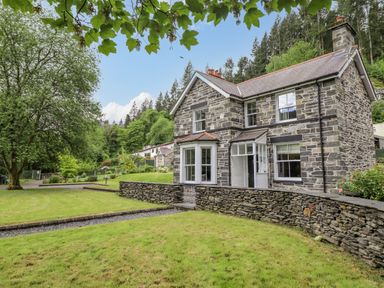 A stone house with a grassy yard and trees around at Craigside in Betws-Y-Coed