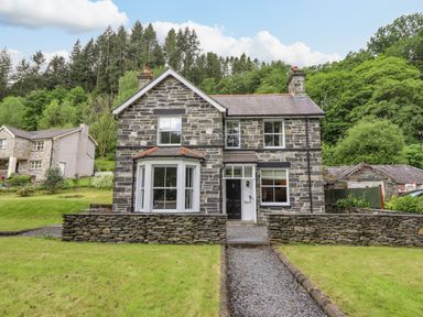 A stone house with a front garden and gravel path surrounded by trees at Craigside in Betws-Y-Coed