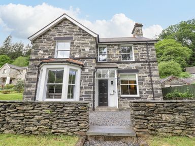 Stone house with black door and white framed windows with stone wall in front at Craigside in Betws-Y-Coed