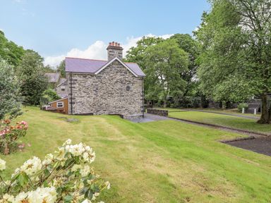 A stone house with a tiled roof surrounded by grass and trees at Craigside in Betws-Y-Coed