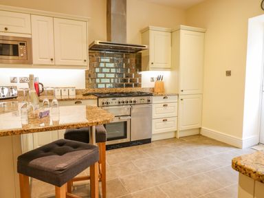 A kitchen with granite countertops, cream cabinetry, a gas stove, microwave, two bar stools, and a tiled floor at Craigside in Betws-Y-Coed