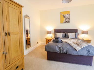 A bedroom with a bed covered with gray bedding and towels two wooden nightstands with lamps a wooden wardrobe and a wall mirror at Craigside in Betws-Y-Coed