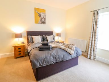 A bedroom with a double bed flanked by two wooden nightstands with lamps and a window with patterned curtains at Craigside in Betws-Y-Coed
