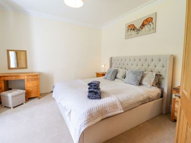 A bedroom with a large bed with pillows and folded towels a wooden desk with a mirror and a small cushioned stool at Craigside in Betws-Y-Coed