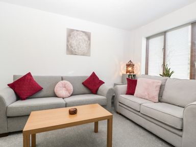 A living room with two grey sofas red and pink cushions wooden coffee table and window blinds at 16 Mythern Meadow in Bradford-On-Avon