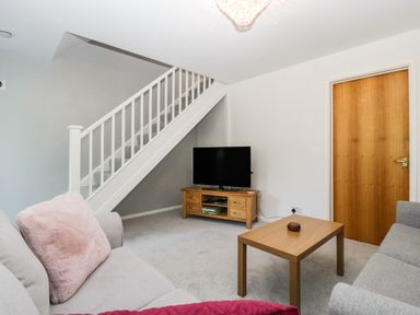 A living room with two sofas a wooden coffee table a television on a wooden stand and stairs at 16 Mythern Meadow Bradford-On-Avon