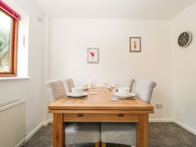 A dining room with a wooden table set with bowls plates and wine glasses four upholstered chairs two framed pictures and a wall clock at 16 Mythern Meadow in Bradford-On-Avon