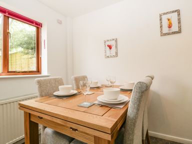 A dining room with a wooden table set with bowls plates and glasses with grey chairs near a window at 16 Mythern Meadow in Bradford-On-Avon