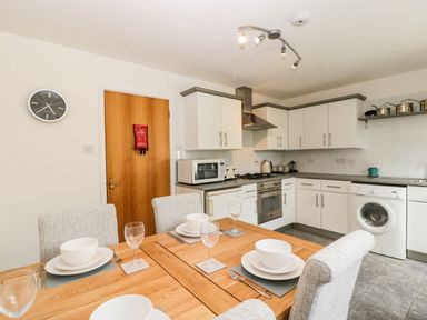 A kitchen with white cabinets dining table with place settings a washing machine and a wooden door at 16 Mythern Meadow in Bradford-On-Avon