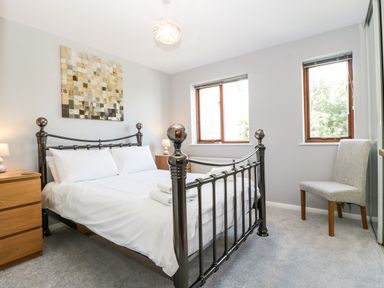 A bedroom with a metal bed frame white bedding two wooden nightstands a chair and two windows at 16 Mythern Meadow Bradford-On-Avon