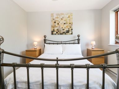 A bedroom with a metal bed frame white bedding two bedside tables with lamps and a window at 16 Mythern Meadow in Bradford-On-Avon