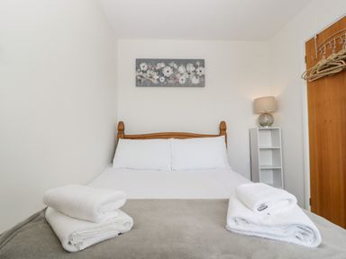 A bedroom with a wooden bed, white bedding, folded white towels, a lamp on a white shelf, and hangers on a wooden door at 16 Mythern Meadow in Bradford-On-Avon