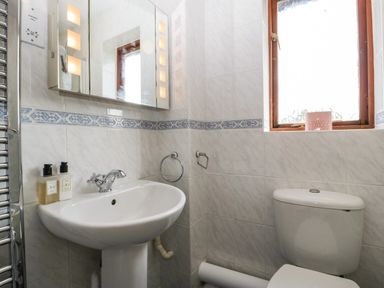 A bathroom with a sink and mirror cabinet above and a toilet below a window at 16 Mythern Meadow in Bradford-On-Avon