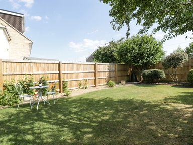 A garden with a lawn a wooden fence and a metal table with two chairs at 16 Mythern Meadow in Bradford-On-Avon
