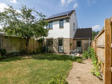 A backyard with a tree a lawn a gravel path wooden fences and a two story house with solar panels at 16 Mythern Meadow in Bradford-On-Avon