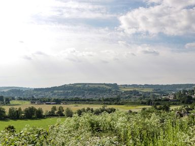 A countryside landscape with green fields trees and hills under a cloudy sky at 16 Mythern Meadow in Bradford-On-Avon