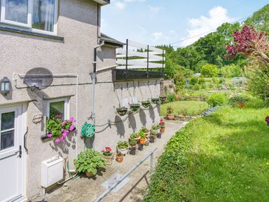 Side of a house with potted plants and hanging flower baskets next to a garden at Kavieng in Glangrwyney near Gilwern