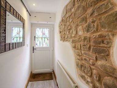 A hallway with a white door with stained glass windows a stone wall a radiator a mirror and a doormat at Kavieng in Glangrwyney near Gilwern