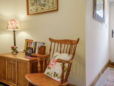 A wooden chair with a floral cushion next to a wooden cabinet with a lamp and books at Kavieng in Glangrwyney near Gilwern
