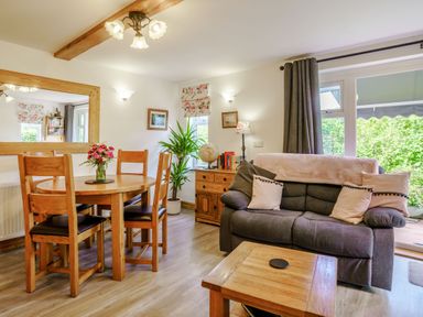 A dining area with wooden table and chairs beside a gray sofa with pillows and a wooden sideboard at Kavieng in Glangrwyney near Gilwern