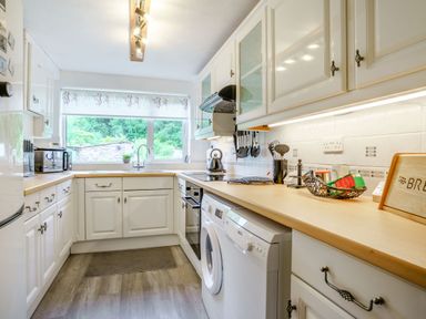 A kitchen with white cabinets washing machine oven and window with a view at Kavieng Glangrwyney near Gilwern