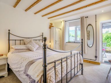 A bedroom with a metal bed frame a white wardrobe a window with curtains an oval mirror and a door leading outside at Kavieng in Glangrwyney near Gilwern