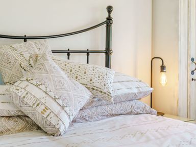 A bed with patterned pillows and bedding with a metal headboard and a lit bedside lamp at Kavieng in Glangrwyney near Gilwern