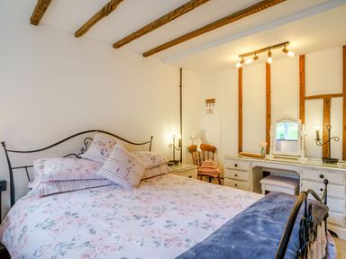 A bedroom with a bed with floral bedding a bedside table a wooden chair with towels and a teddy bear and a dresser with a mirror at Kavieng Glangrwyney near Gilwern