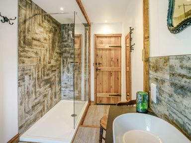 A bathroom with a walk-in shower and patterned wall tiles a wooden door and a sink with a green candle at Kavieng in Glangrwyney near Gilwern