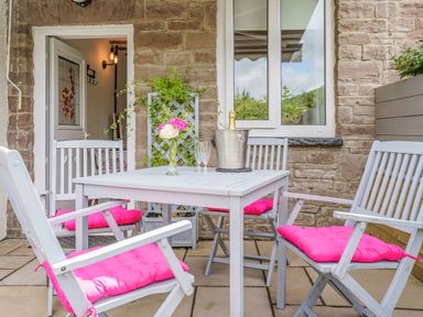 An outdoor patio area with a white table and four chairs with pink cushions a vase with flowers on the table and a champagne bottle in an ice bucket at Kavieng Glangrwyney near Gilwern