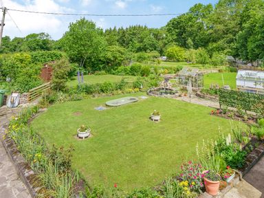 A garden with greenhouses flower beds and a lawn at Kavieng Glangrwyney near Gilwern
