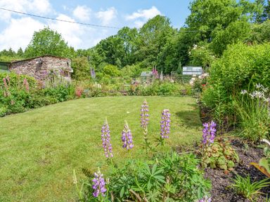 A garden with purple flowers a stone shed and greenhouses surrounded by trees at Kavieng in Glangrwyney near Gilwern
