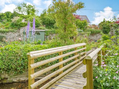 A wooden bridge over a small stream with a garden shed and stone wall in the background at Kavieng in Glangrwyney near Gilwern