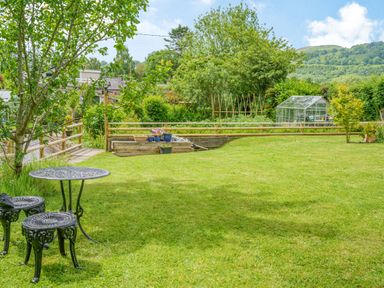 A garden with grass lawn metal table and chairs greenhouse and plants at Kavieng in Glangrwyney near Gilwern