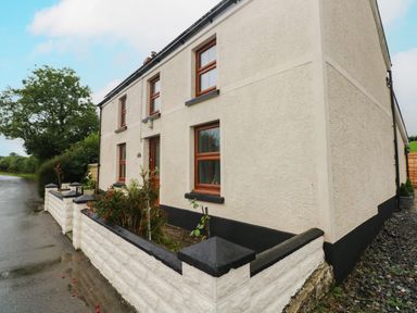Exterior of a two-story house with white walls and wooden framed windows surrounded by a low white wall at Brynawel in Llangynin near Llanboidy