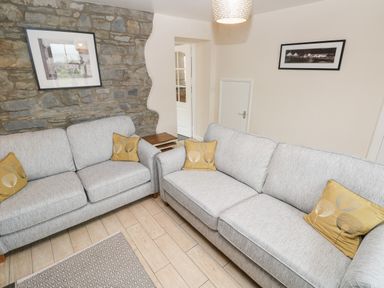 A living room with two grey sofas with yellow cushions and a stone wall at Brynawel in Llangynin near Llanboidy