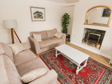 A living room with beige sofas white coffee table red patterned rug fireplace and a tall floor lamp at Brynawel in Llangynin near Llanboidy