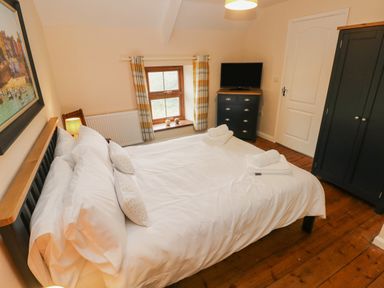 A bedroom with a bed a dresser a wardrobe a window with curtains and a door at Brynawel in Llangynin near Llanboidy