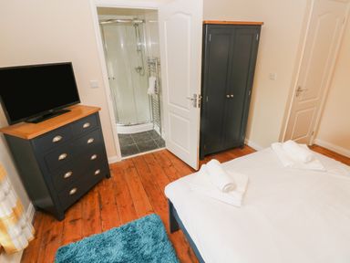 A bedroom with a bed, chest of drawers with a television, wardrobe, blue rug, and a door leading to a bathroom at Brynawel in Llangynin near Llanboidy