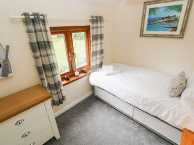 A small bedroom with a single bed with white bedding beside a window with checked curtains and a wooden dresser Brynawel in Llangynin near Llanboidy