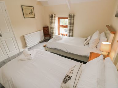 A bedroom with two single beds a bedside table with a lamp a window with plaid curtains a wooden chair and a radiator at Brynawel in Llangynin near Llanboidy