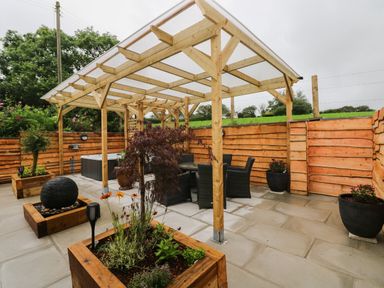 An outdoor patio with a wooden pergola a dining table with chairs planters with plants and a water feature at Brynawel in Llangynin near Llanboidy