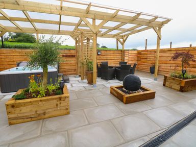 A patio with wooden planters a hot tub a dining table with chairs and a pergola at Brynawel in Llangynin near Llanboidy