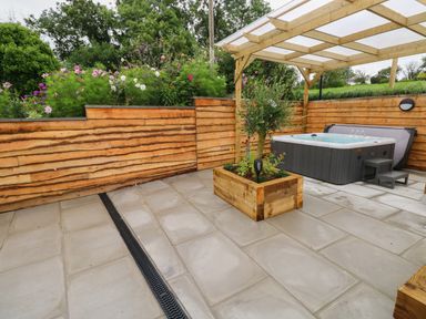 An outdoor patio area with a hot tub under a wooden pergola and a wooden planter with a small tree at Brynawel in Llangynin near Llanboidy