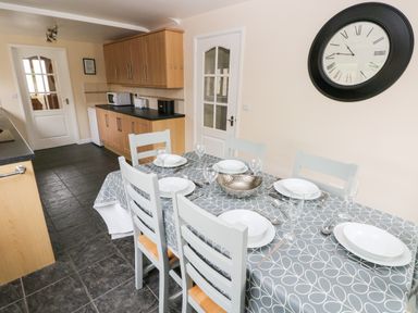 A kitchen with a dining table set with plates glasses and cutlery and wooden cabinets on one side at Brynawel in Llangynin near Llanboidy